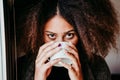 portrait of beautiful afro american young woman by the window drinking tea or coffee. Lifestyle indoors Royalty Free Stock Photo