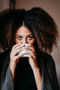 portrait of beautiful afro american young woman by the window drinking tea or coffee. Lifestyle indoors Royalty Free Stock Photo