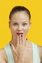 Portrait of a beautiful amazed young woman with hand over mouth over yellow background Royalty Free Stock Photo