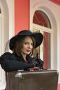 Portrait of beautiful aristocratic woman in black wide-brimmed hat and lace gloves with retro suitcase. Female traveler