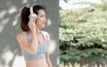 Portrait Beautiful Asian adult sportive woman wearing sport bra, resting, putting headphone to listen music with happiness and