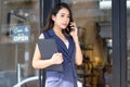 Portrait of beautiful Asian casual businesswoman talking by smartphone while standing in front cafe. Young entrepreneur making Royalty Free Stock Photo