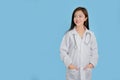 Portrait of a beautiful Asian female doctor is smiling. She stands is isolated on blue background