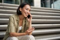 Portrait of beautiful asian girl talks on mobile phone, sits on street stairs. Woman with smartphone smiling, making a Royalty Free Stock Photo