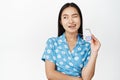 Portrait of beautiful asian modern girl biting temple of sunglasses, winking and smiling with confidence, standing over Royalty Free Stock Photo