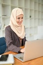 A portrait of a beautiful Asian Muslim businesswoman in hijab focuses on her work on her laptop Royalty Free Stock Photo