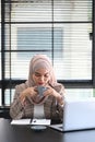 Portrait of a beautiful asian muslim woman is working on laptop and drinking hot beverage. Royalty Free Stock Photo