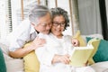 Portrait of beautiful Asian senior couple reading together interesting book while sit on couch in living room at home. Old couple Royalty Free Stock Photo