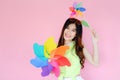 Portrait beautiful asian teen girl beaming smile on pink background, fashion summer set with colorful wind turbine or pinwheel or
