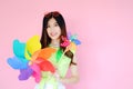 Portrait beautiful asian teen girl beaming smile on pink background, fashion summer set with colorful wind turbine or pinwheel or