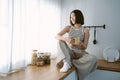 Portrait of beautiful Asian woman in cozy clothes relax sitting on counter top at kitchen drinking coffee and looking through Royalty Free Stock Photo