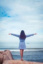 A portrait of beautiful asian woman in dress back stand, hands to the sides on a stone by the sea