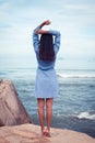 A portrait of beautiful asian woman in dress back stand and rise hands on a stone by the sea
