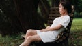 Portrait of beautiful Asian woman sitting on bench in summer forest, Chinese girl in white dress sleeping with eyes closed Royalty Free Stock Photo