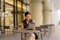 Portrait of beautiful Asian woman sitting outdoors at coffee shop restaurant smiling and using digital tablet computer Royalty Free Stock Photo