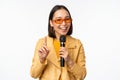 Portrait of beautiful asian woman in sunglasses, stylish girl singing, giving speech with microphone, holding mic and Royalty Free Stock Photo