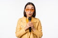 Portrait of beautiful asian woman in sunglasses, stylish girl singing, giving speech with microphone, holding mic and Royalty Free Stock Photo