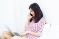 Portrait of beautiful asian young woman setting on bed using laptop computer and talk smart phone at bedroom for leisure and relax Royalty Free Stock Photo