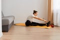 Portrait of beautiful athletic woman wearing white t shirt and black leggins doing sport exercises at home, bending to touch feet Royalty Free Stock Photo