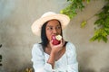 Portrait of a beautiful black girl with a white blouse and a hat eating an apple Royalty Free Stock Photo