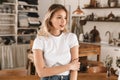 Portrait of beautiful blond girl smiling and rejoicing while standing in stylish wooden kitchen at home