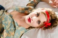 Portrait of beautiful blond pinup girl in floral shirt having fun relaxing lying on back in white bed