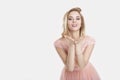 Portrait of beautiful blond woman in pink cocktail dress doing kiss on grey background Royalty Free Stock Photo