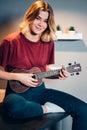 Portrait of beautiful blond woman playing ukulele at home on table Royalty Free Stock Photo