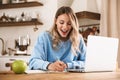 Portrait of beautiful blond woman 20s wearing casual sweatshirt working on laptop and writing down notes at home Royalty Free Stock Photo