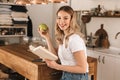 Portrait of beautiful blond woman reading book and drinking tea while standing in stylish wooden kitchen at home Royalty Free Stock Photo