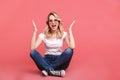 Portrait of beautiful blond woman 20s wearing vintage sunglasses laughing while sitting on floor with legs crossed Royalty Free Stock Photo