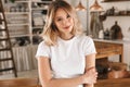 Portrait of beautiful blond woman smiling and rejoicing while standing in stylish wooden kitchen at home