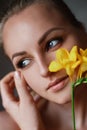 Portrait of a beautiful blonde with blue-green eyes and a flower of yellow fresia in her hair. A young woman holds both