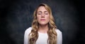 Portrait of a beautiful blonde dramatically closing her eyes on a dark background.