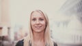 Portrait of beautiful blonde girl looking at camera and smiling. Young attractive woman on the blur city background.