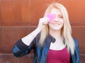 Portrait of a beautiful blonde girl with one hand closes the eyes pink paper heart. Filter, light leak effect.