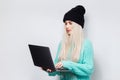 Portrait of beautiful blonde girl using laptop on white background. Wearing blue sweater and black hat. Royalty Free Stock Photo