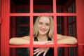 Portrait of Beautiful blonde hair girl on black dress standing in red phone booth against black wall as portrait fashion pose outd Royalty Free Stock Photo