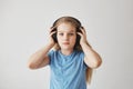 Portrait of beautiful blonde little girl with long hair and blue eyes wearing big headphones, holding it with hands Royalty Free Stock Photo