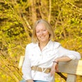 Portrait of a beautiful blonde middle-aged woman in the park on the bench.