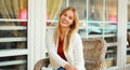 Portrait of beautiful blonde smiling young woman sitting on chair waiting in city cafe Royalty Free Stock Photo