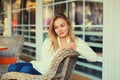 Portrait of beautiful blonde smiling young woman sitting on chair waiting in city cafe Royalty Free Stock Photo