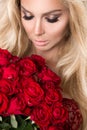 Portrait of the beautiful blonde woman and amazing looks and long hair, perfect skin, keeps the face of a bouquet of red roses , v Royalty Free Stock Photo