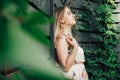 Portrait of a beautiful blonde woman dressed in flower dress in a green leaves trees on a wooden wall background. Copy, empty Royalty Free Stock Photo