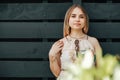 Portrait of a beautiful blonde woman dressed in flower dress in a green leaves trees on a wooden wall background. Copy, empty