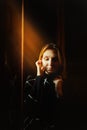 Portrait of a beautiful blonde woman, who is sitting alone in the evening near the window, illuminated by a ray of sunlight. The Royalty Free Stock Photo