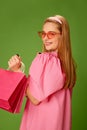 Portrait of beautiful blonde young girl in cute pink dress and trendy sunglasses posing with shopping bags over green Royalty Free Stock Photo