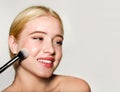 Portrait of beautiful blonde young woman face holding make up brushes. Spa model girl with clean skin isolated on a gray Royalty Free Stock Photo