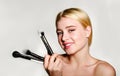 Portrait of beautiful blonde young woman face holding make up brushes. Spa model girl with clean skin isolated on a gray Royalty Free Stock Photo