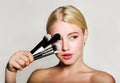 Portrait of beautiful blonde young woman face holding make up brushes. Spa model girl with fresh clean skin  on a white Royalty Free Stock Photo